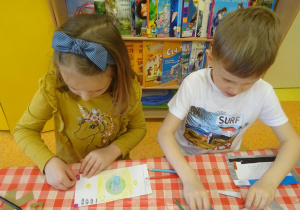 Czwórka dzieci projektu swój banknot, rysują kredkami, nakleja elementy papierowe.